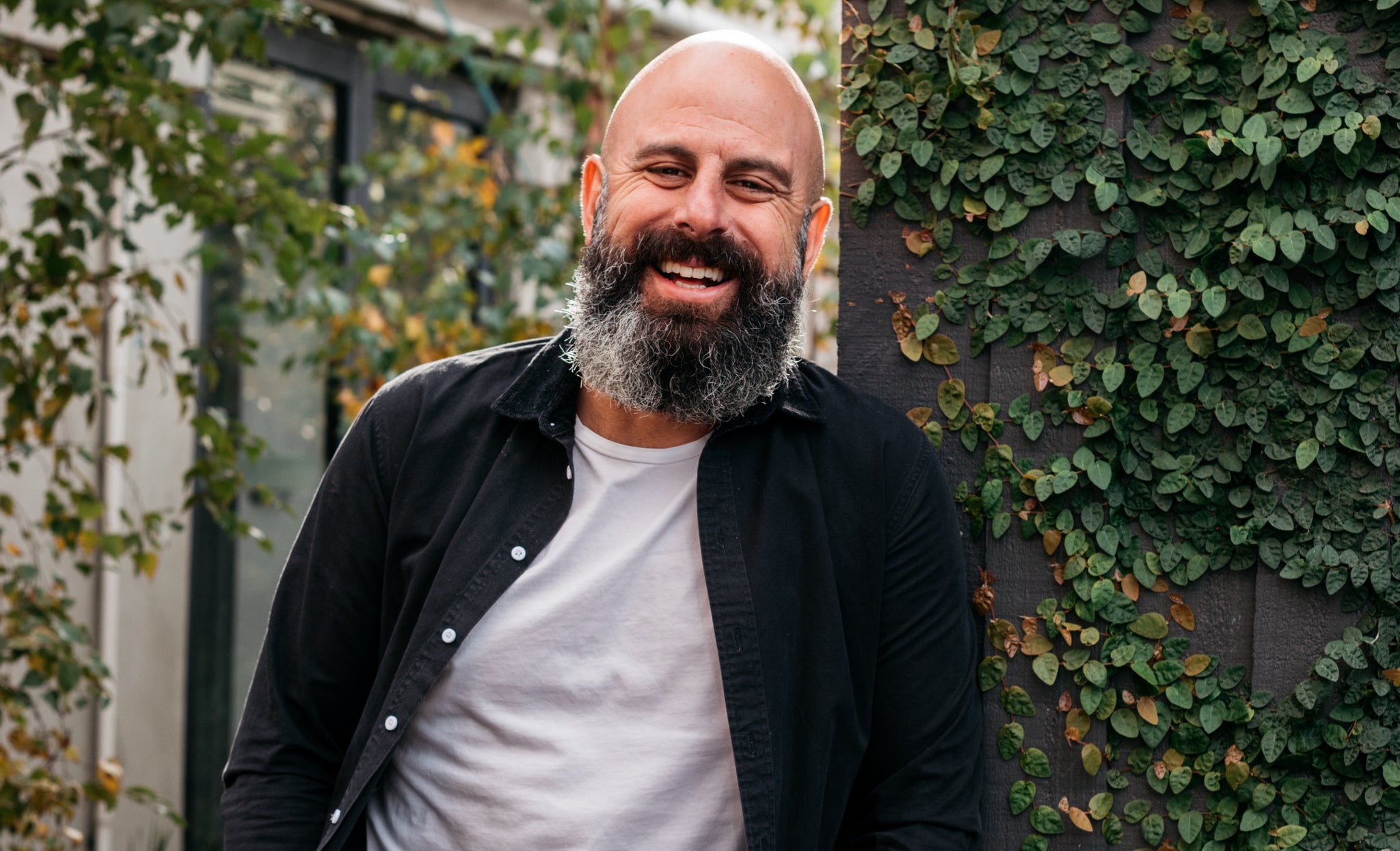 Pana Barbounis, founder of vegan chocolate brand Pana Organic is standing against a leafy background smiling. The title reads LOM x PANA ORGANIC