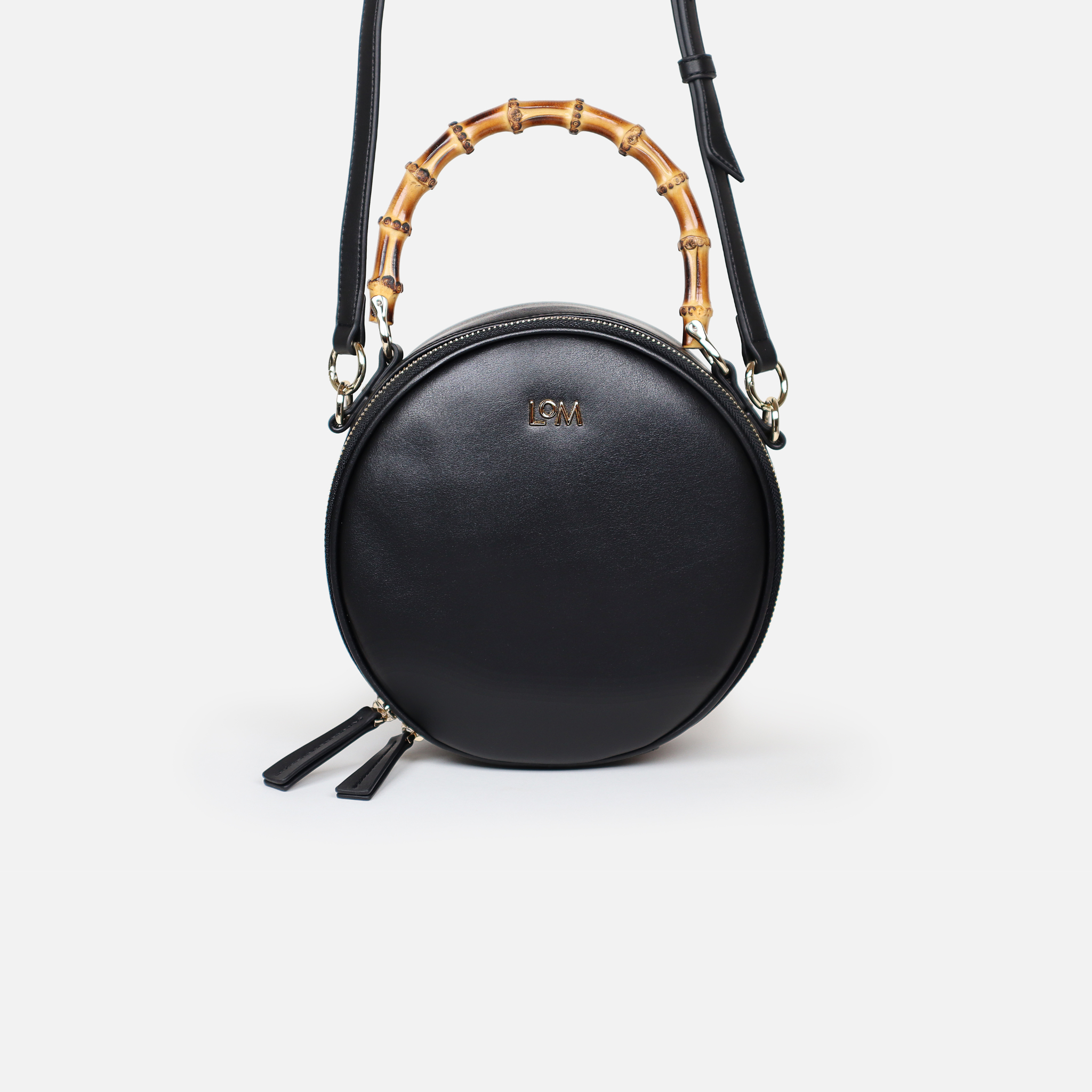 Circular handbag with bamboo handle and long shoulder strap attached.. Made from premium black cactus leather, light gold hardware, black organic cotton lining.
