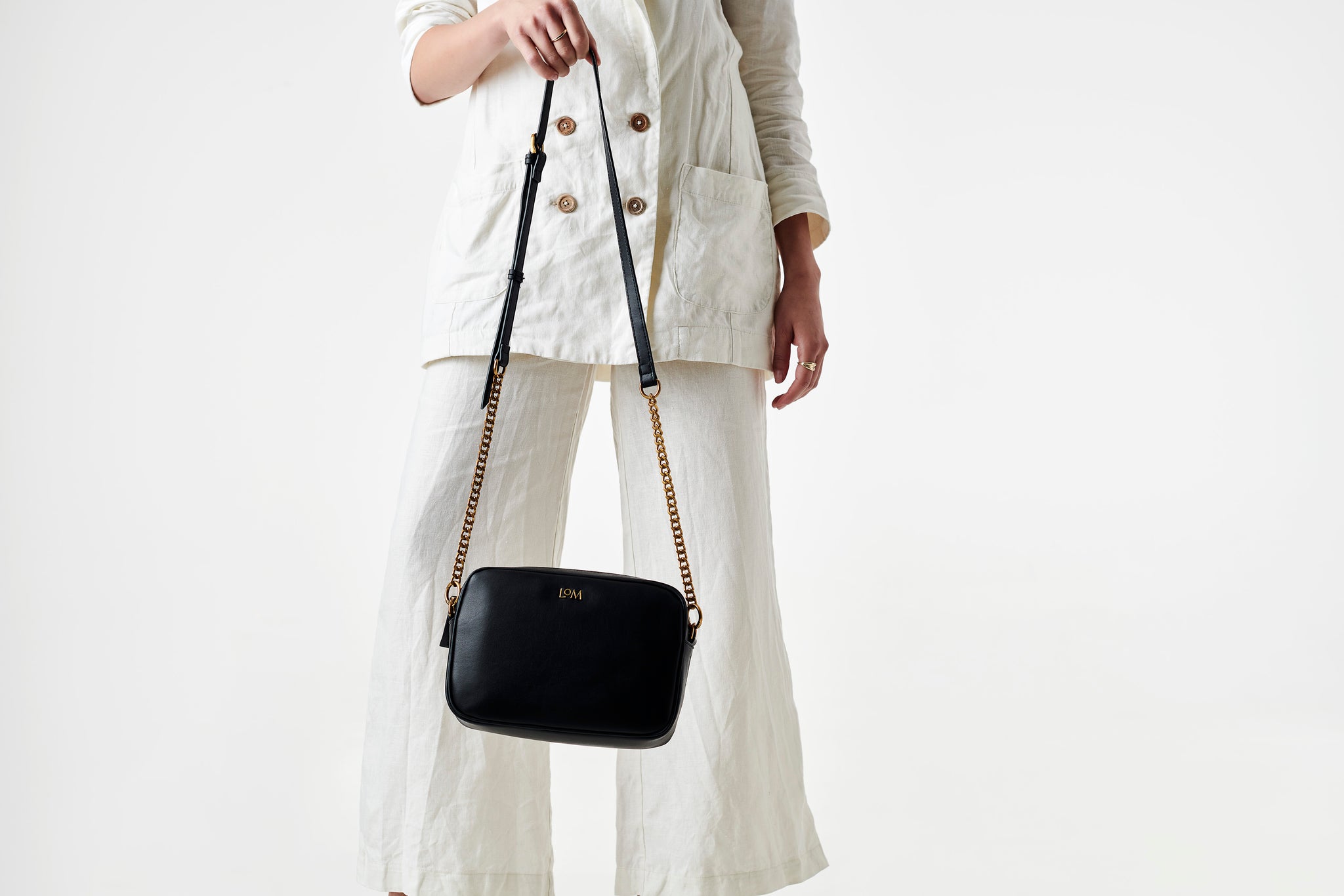 LOM Austrlia | Model holds Libra Cross Body bag in sustainable, vegan, black cactus leather with antique gold hardware.